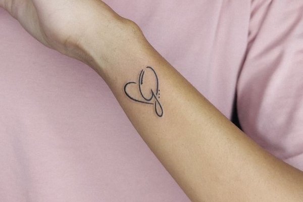 Tattoo mit einem filigranen Buchstaben und kleinem Herz auf dem Handgelenk