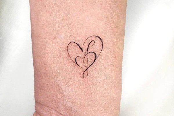 Tattoo mit einem filigranen Buchstaben und kleinem Herz auf dem Handgelenk