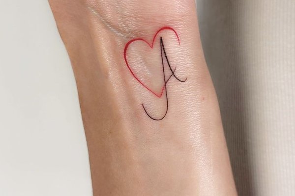 Tattoo mit einem filigranen Buchstaben und kleinem Herz auf dem Handgelenk