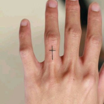 Kleines schwarzes Kreuz Tattoo an der Fingerwurzel