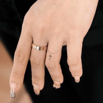 Kleines schwarzes Kreuz Tattoo an der Fingerwurzel