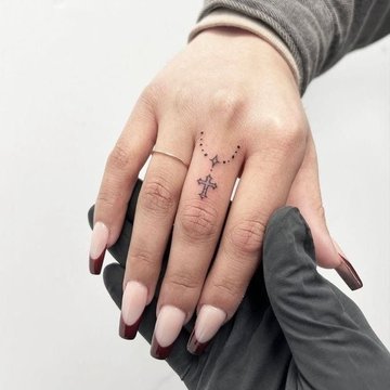 Kleines schwarzes Kreuz Tattoo an der Fingerwurzel